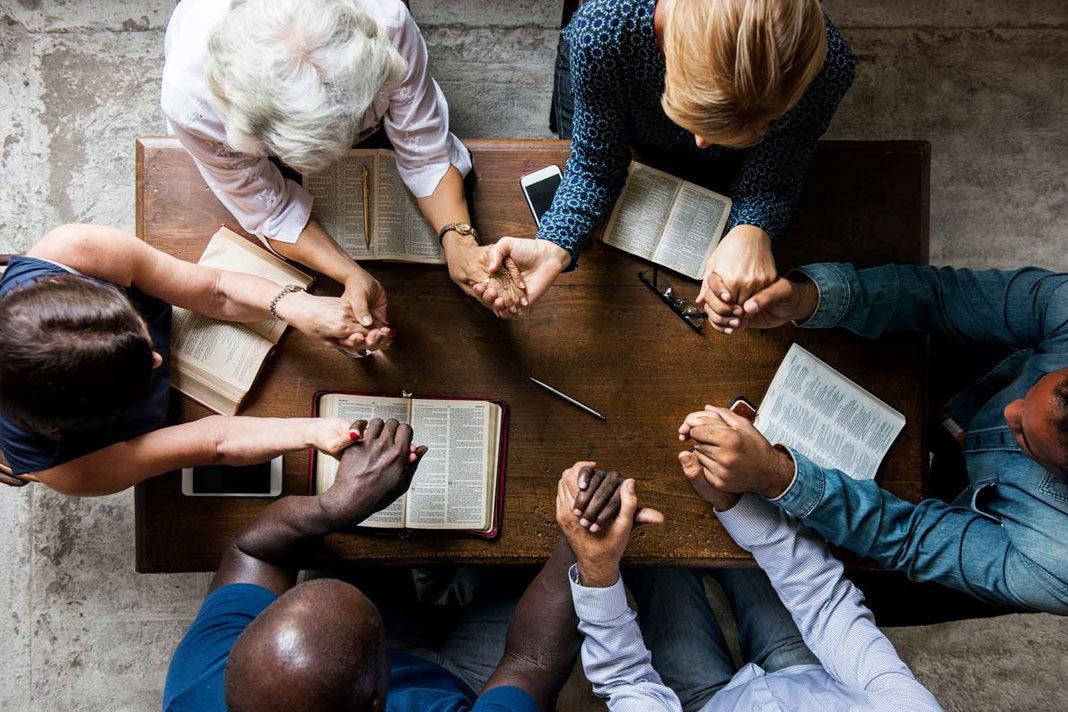 People gathered around a table with open Bibles in prayer